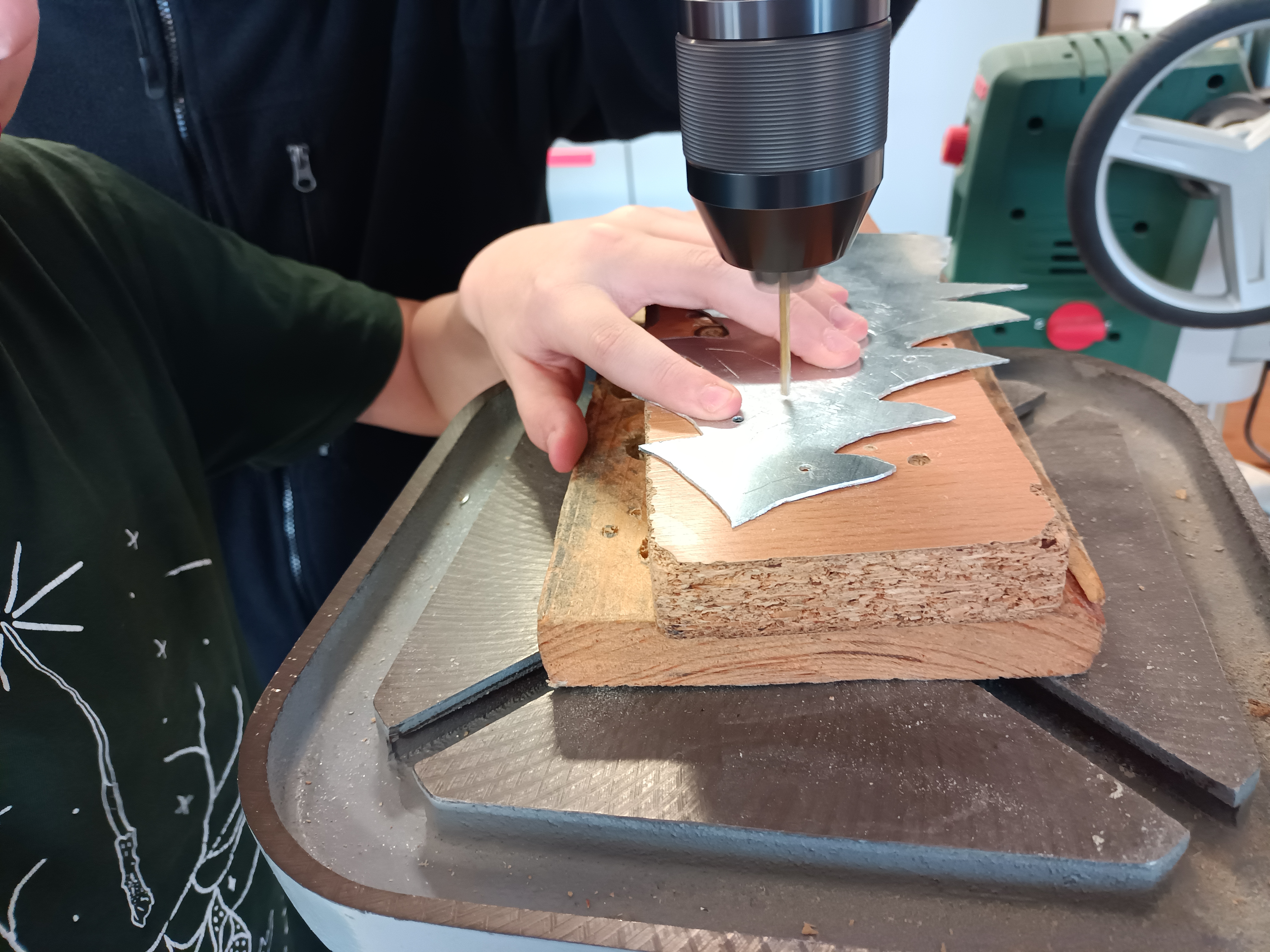 Schüler bohrt mit einer Säulenbohrmaschine ein aus Blech ausgesägtes Weihnachtsbaum-Motiv, weihnachtliches Werkstück aus dem Technikraum.