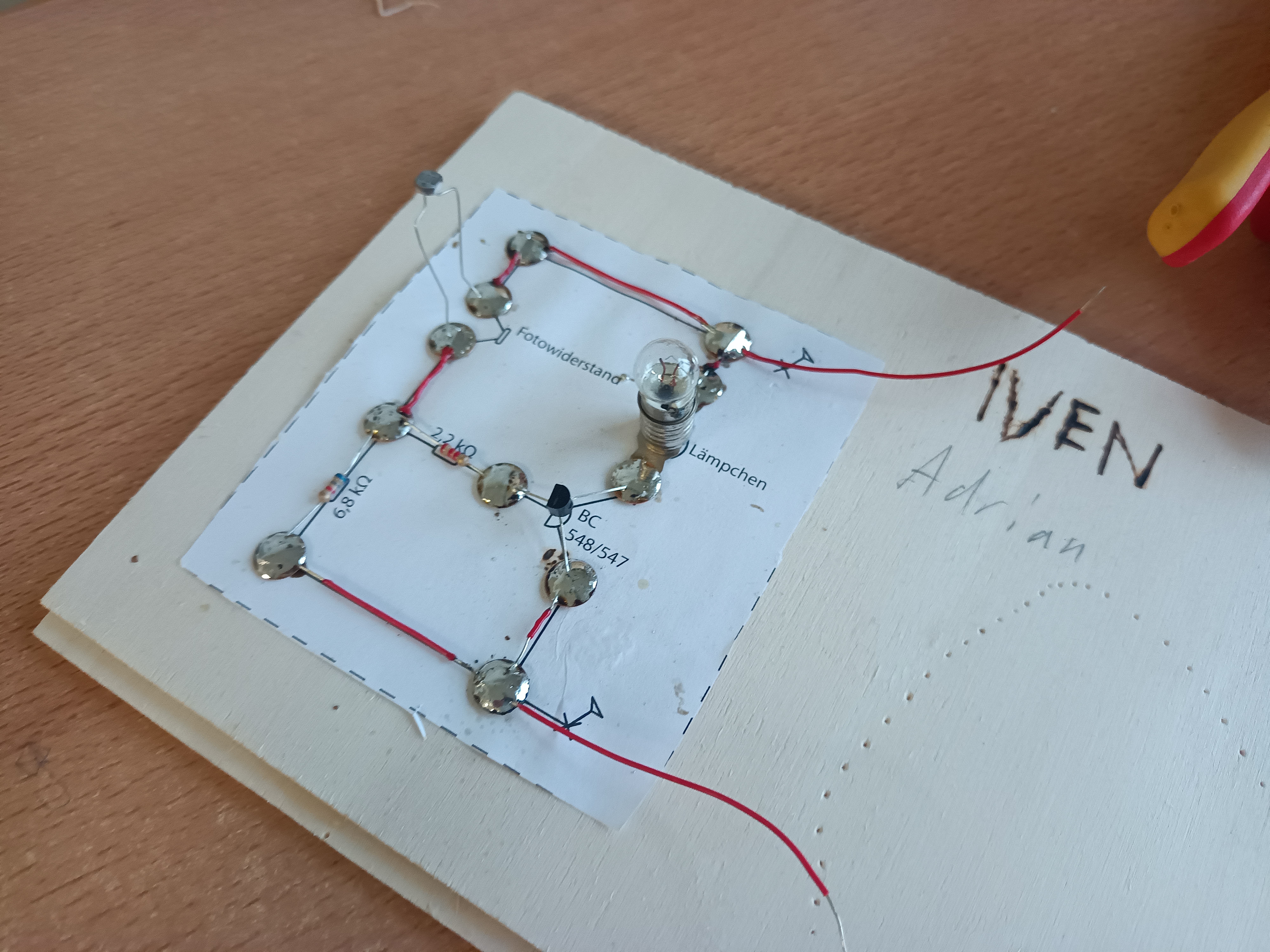 Selbst gelötete elektronische Schaltung mit Fotowiderstand, Transistor und Glühlämpchen auf einer Holzplatte, Elektrotechnik Stufe 9.