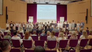 Schüler:innen der Klasse 9a bei der Preisverleihung des Bonner Demokratiepreises, auf dem Bildschirm im Hintergrund der 3. Preis in der Kategorie Film/Theater für das Projekt „Malala Yousafzai“